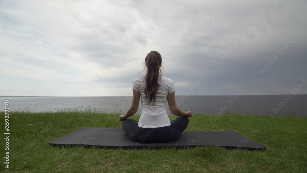 Young fit woman practice yoga on coast near the lake or sea. Woman sitting in lotus pose and meditating Young fit woman practice yoga on coast near the lake or sea. Woman sitting in lotus pose and meditating