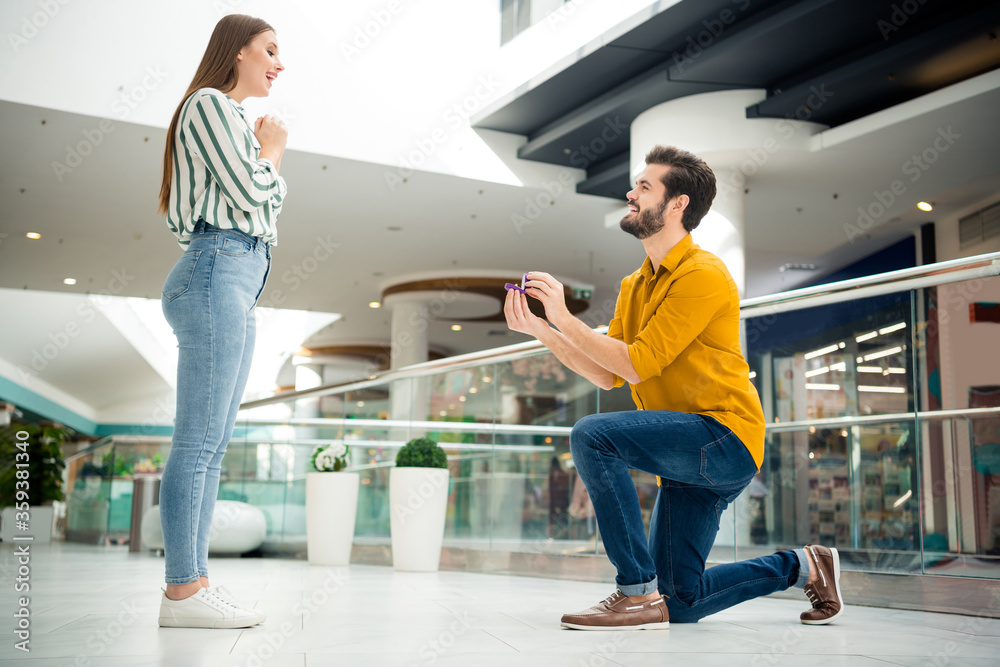 Obraz premium Will you marry me Full length profile side photo of two people man kneeling propose romance amazed shocked girl give her jewelry ring in shopping mall center