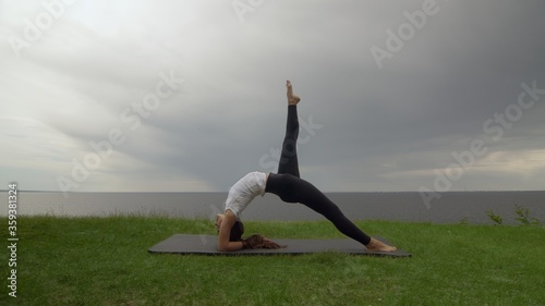 Young fit woman practice yoga on coast near the lake or sea. Woman doing Inverted Staff Dvi Pada Viparita Dandasana pose