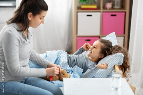 family, health and people concept - mother and happy smiling little daughter lying in bed at home