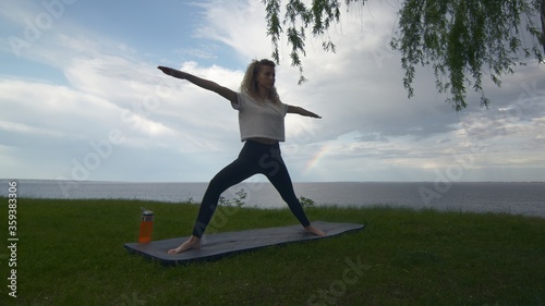 Young fit woman practice yoga on coast near the lake or sea. Woman doing Warrior II pose