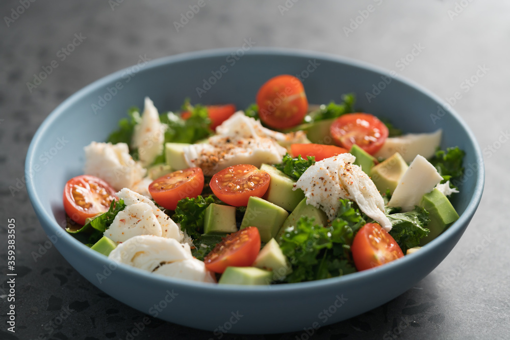 Salad with avocado, mozzarella, tomatoes and kale in blue ceramic bowl
