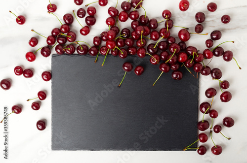 Top view of darl slate plate and ripe cherries on the white marble kitchen table photo