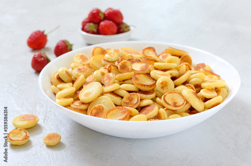 Pancake cereal in a bowl with fresh strawberries on a light background. Tasty and trendy breakfast. Organic Dutch Mini-Pancakes. Foods trend Pancake cereal in a bowl with fresh strawberries on a light background. Tasty and trendy breakfast. Organic Dutch Mini-Pancakes. Foods trend