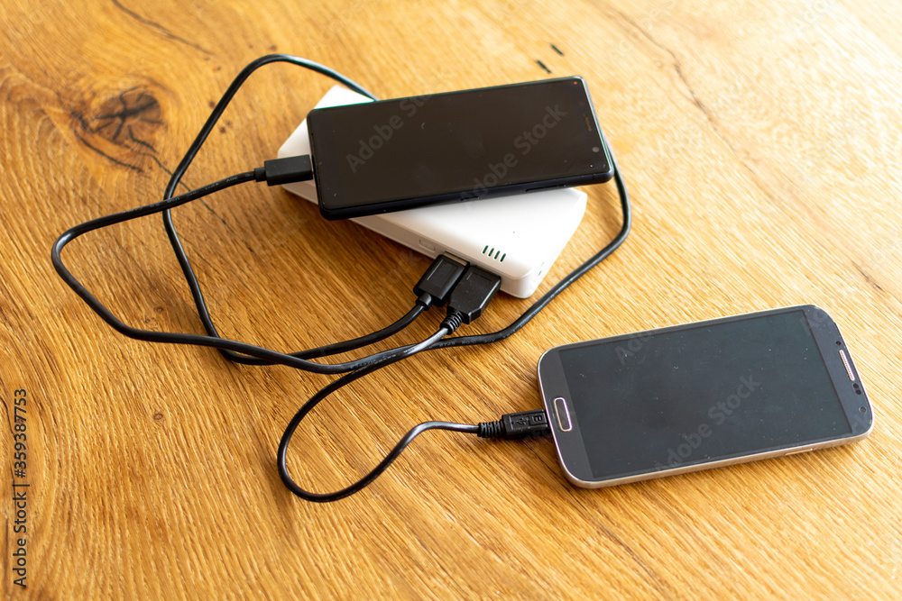 Two Mobile Phone sharing USB Power Bank on a wooden Table to charge the mobile devices Two Mobile Phone sharing USB Power Bank on a wooden Table to charge the mobile devices