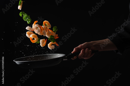 Fényképezés Shrimps with parsley frying in a pan, the chef cooks, freezing in motion on a bl
