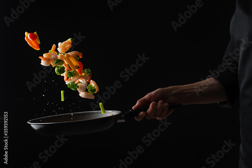 Cooked seafood, vegetables with shrimps are fried in a pan, frozen in motion, on a black background, restaurant menu