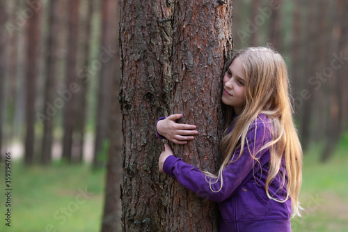 Blond girl huggies tree in the pine forest, enjoying nature. Love nature and care of nature concept.