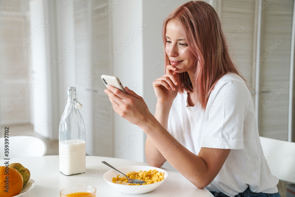 Photo of young cheerful woman using cellphone while having breakfast Photo of young cheerful woman using cellphone while having breakfast