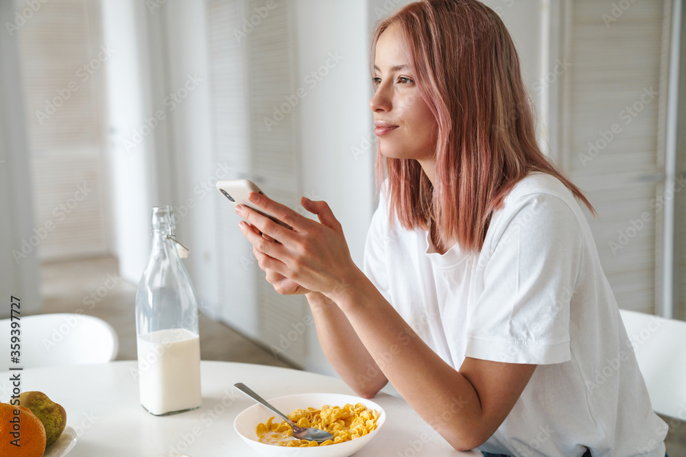 Photo of young caucasian woman using cellphone while having breakfast