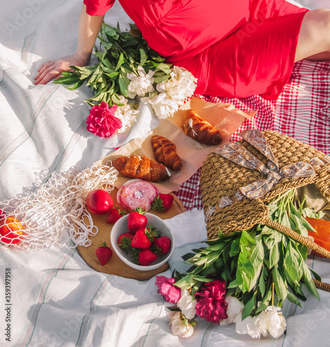 picnic pregnancy table. pregnant woman in red dress is sitting on the tablecloth with fruits, croissants and flowers in basket. picnic concept, free space