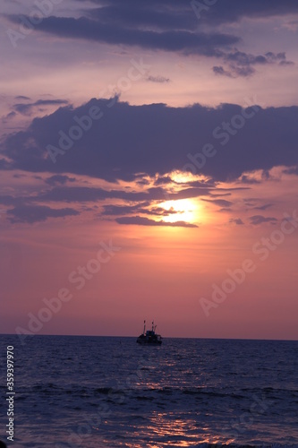 Ship sailing in the ocean with sunset and rays of the sun.