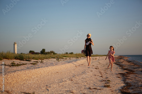 Smiling mother and beautiful daughter having fun on the beach. Portrait of happy woman giving a piggyback ride to cute little girl with copy space. Portrait of kid and her mom during summer