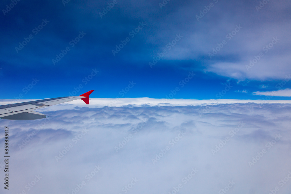 Fototapeta premium The wing of the plane flies over white clouds, the background is blue sky, view through the window.