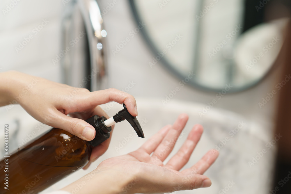 Woman washing hands with soap dispenser bottle at sink in bathroom.