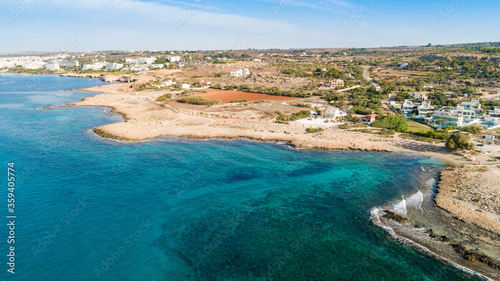 Fototapeta premium Aerial bird's eye view of Ammos tou Kambouri beach, Ayia Napa, Cavo Greco, Famagusta, Cyprus. Tourist attraction bay, rocky beach with golden sand, sunbeds, sea restaurant in Agia Napa from above.