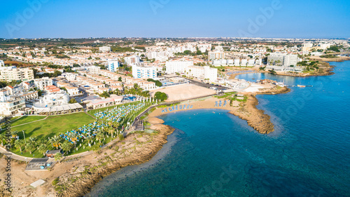 Aerial bird's eye view of Pernera beach in Protaras, Paralimni, Famagusta, Cyprus. Tourist attraction golden sandy bay with sunbeds, water sports, hotels, restaurant, people swimming in sea from above