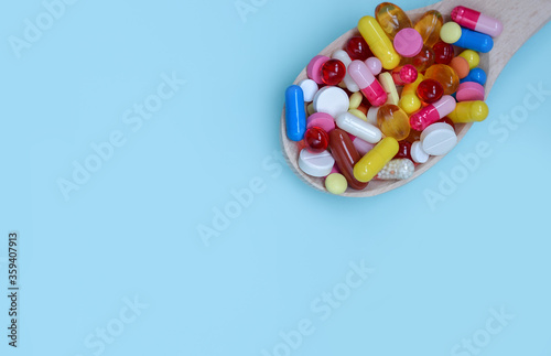 Colorful assorted pharmaceutical medicine capsules   tablets and pills in wooden spoon isolated on blue background. Dietary supplement healthcare product.Copy space for text.