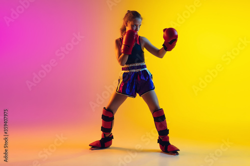 Little caucasian girl  kick boxer on gradient background in neon light  active and expressive. Concept of motion  action  motivation  childhood. Training winner  emotional. Sales  ad  copyspace.