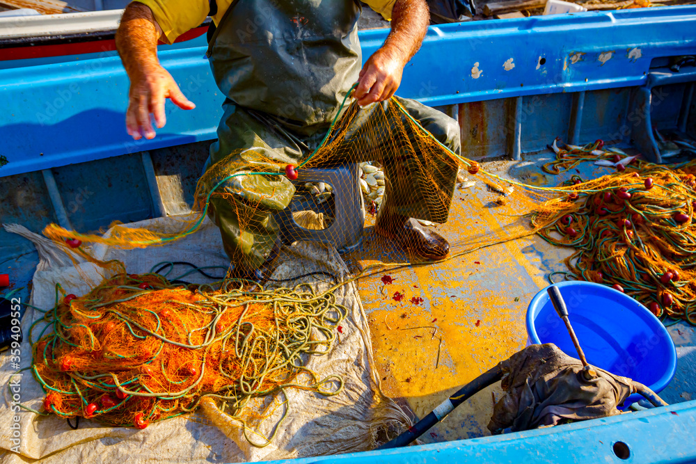 Fisherman is empty fish from net in his small boat