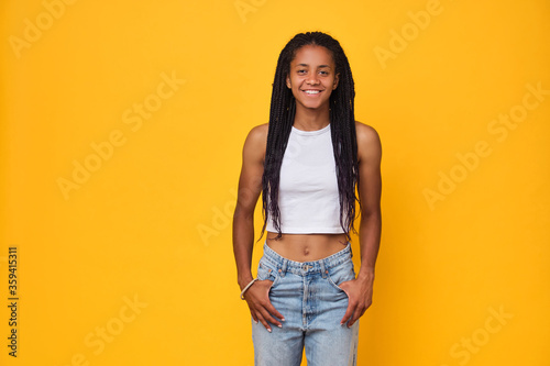 Valokuva Young happy dark skinned teenager girl in white T-shirt athletic body isolated on a yellow background