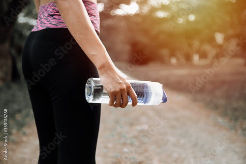 Female runner standing outdoors holding water bottle, healthy and sport concept.