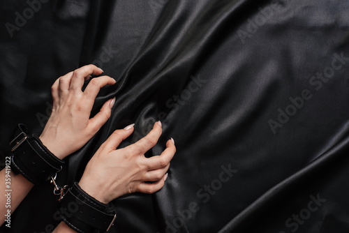 female hands in handcuffs on a dark silk sheet