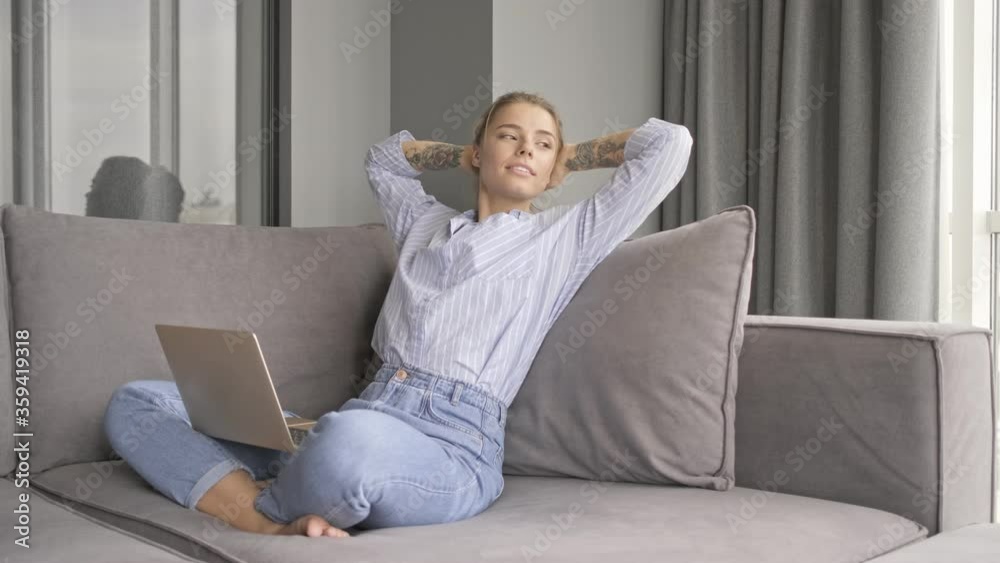 A positive relaxed woman is using her laptop computer while sitting on the sofa in the living room A positive relaxed woman is using her laptop computer while sitting on the sofa in the living room
