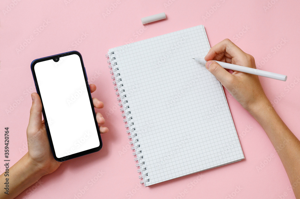 The right hand holds a pen over a notebook sheet. Left hand holds a mobile phone with a blank display The right hand holds a pen over a notebook sheet. Left hand holds a mobile phone with a blank display