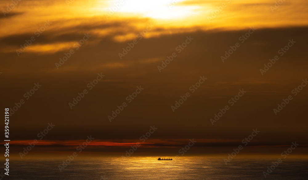Dramatic golden sunset over ocean with cargo ship in the distance.