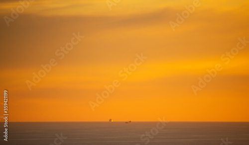 Dramatic golden sunset over ocean with cargo ships in the distance. © Global News Art