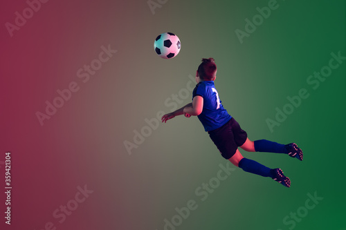 Teen male football or soccer player on gradient background in neon light. Caucasian expressive boy training, practicing on the run, in jump. Concept of sport, competition, winning, motion, action.