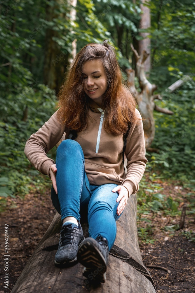 A young brunette girl walks through a dense green forest and sits down on a fallen tree in the middle of the road A young brunette girl walks through a dense green forest and sits down on a fallen tree in the middle of the road