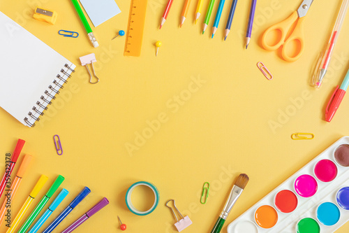 Concept back to school. School stationery flat lay: watercolor, notebook, pens, pencils, sharpener, scissors, ruler, paper clips on yellow background. Copyspace.