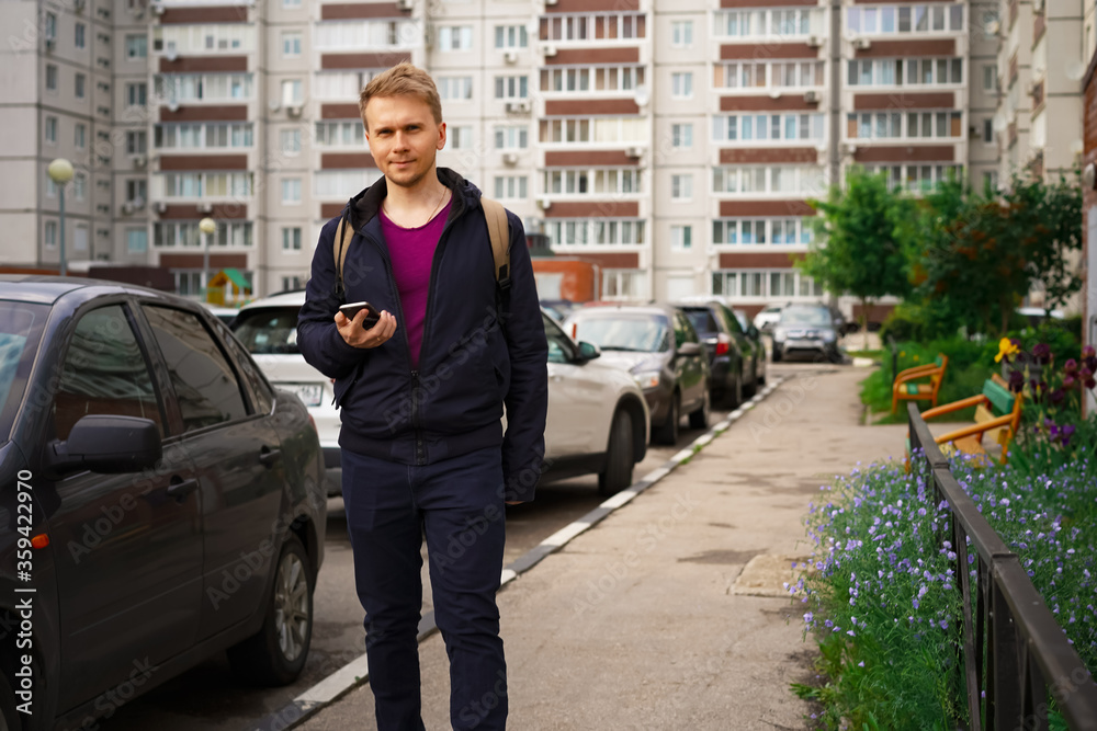 A young blond man with a backpack looks at his smartphone on the streets of the city