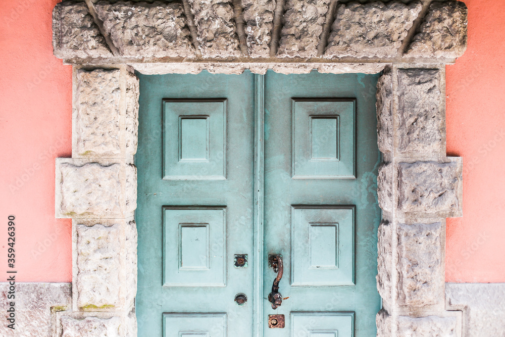A turquoise blue old textured door, front view of a pink building