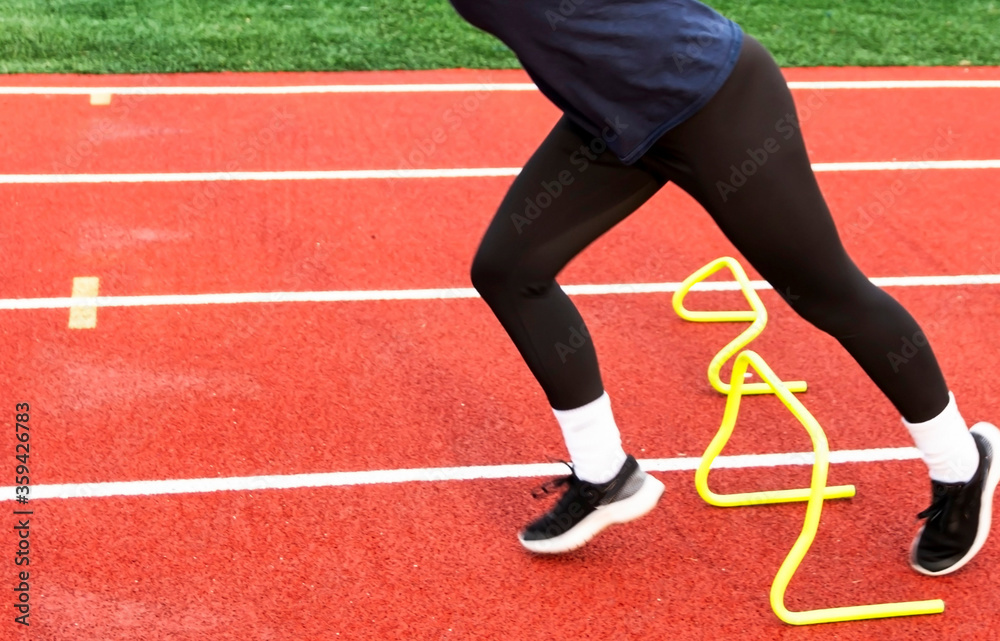 Runners lower body running over yellow mini hurdle Runners lower body running over yellow mini hurdle