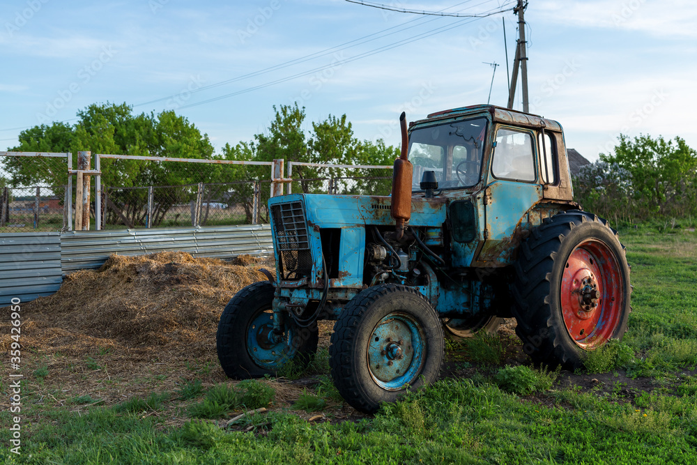 Obraz premium Abandoned old tractor in the village. Blue tractor with red wheel