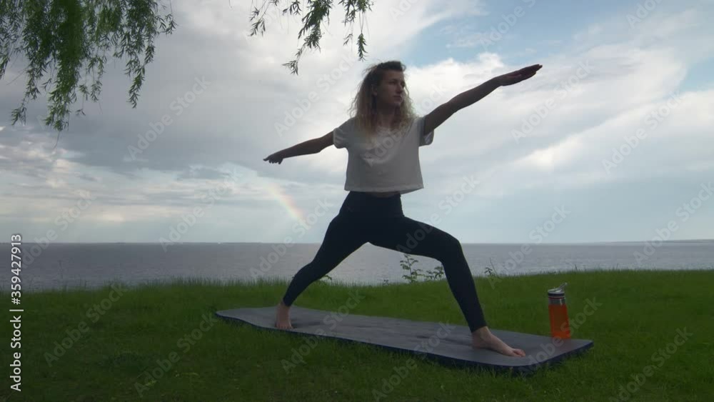 Young fit woman practice yoga on coast near the lake or sea. Woman doing Warrior one and two Poses Young fit woman practice yoga on coast near the lake or sea. Woman doing Warrior one and two Poses