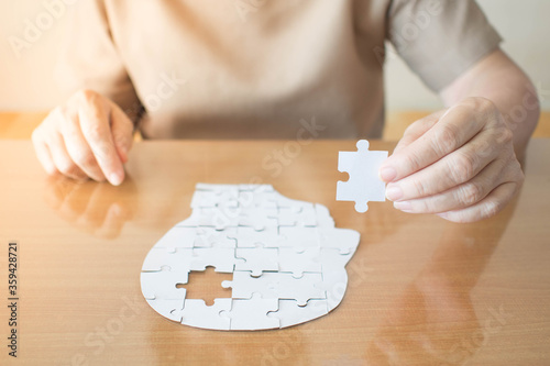 Elderly woman hands holding missing white jigsaw puzzle piece down into the place as a human head brain shape. Creative idea for memory loss, dementia, Alzheimer's disease and mental health concept. photo