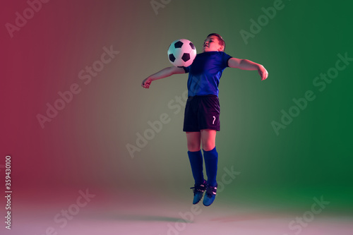 Emotions. Teen male football or soccer player on gradient background in neon light. Caucasian boy training, practicing on the run, in jump. Concept of sport, competition, winning, motion, action. © master1305
