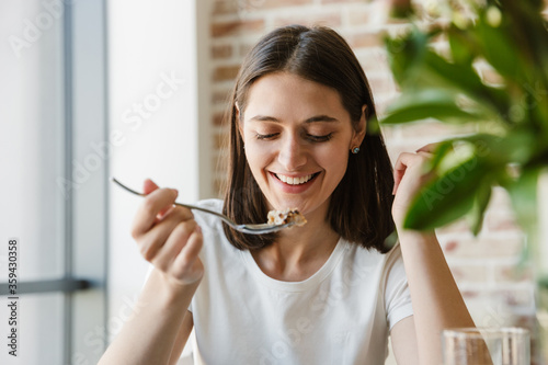 Smiling lovely brunette girl eating healthy breakfast