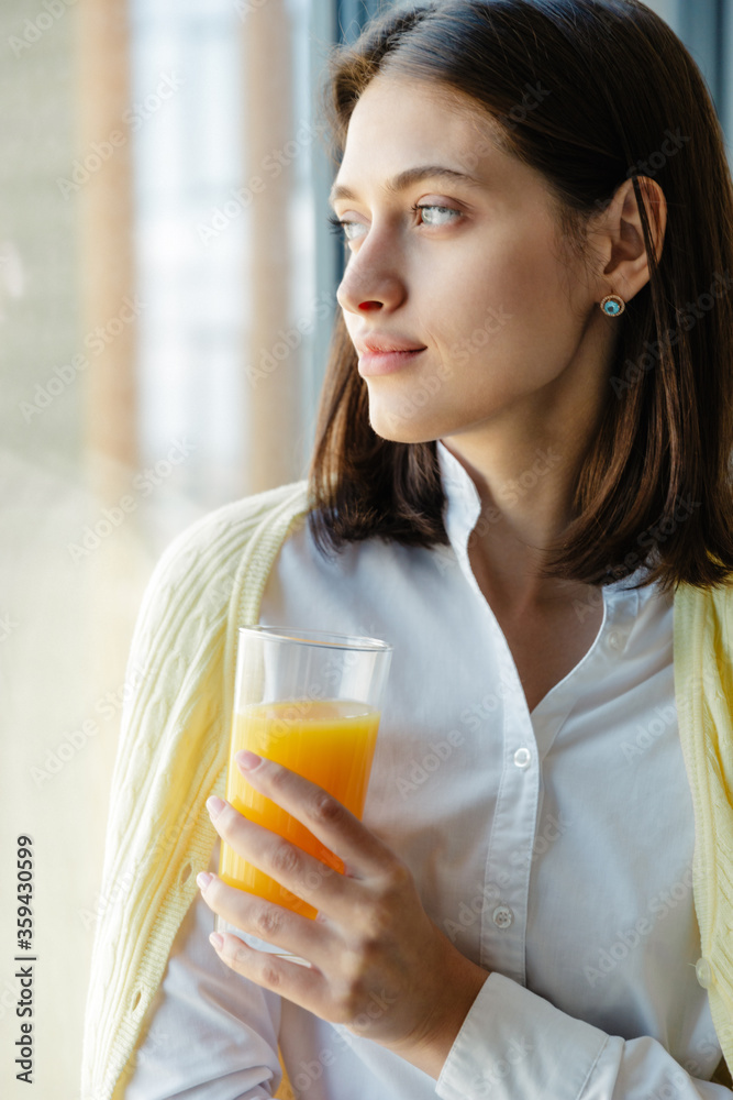 Attractive young brunette woman standing at the window at home Attractive young brunette woman standing at the window at home