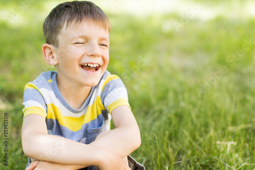 Happy smiling little boy sitting on green grass in park.