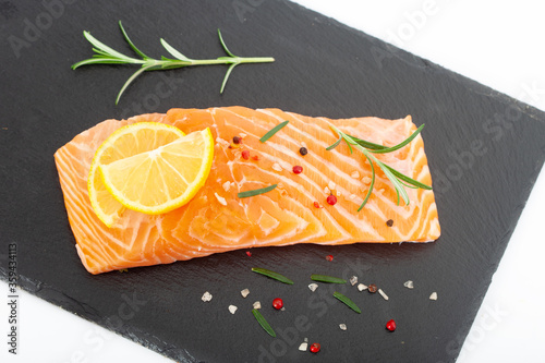 Fresh raw salmon fillet with rosemary and lemon. Salmon steak with seasonings on black plate.