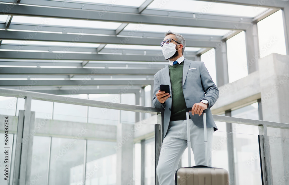 Businessman with luggage going on business trip, wearing face mask at the airport.