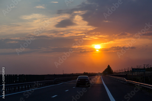 Road trip at sunset, orange sky in the evening, a car on the road