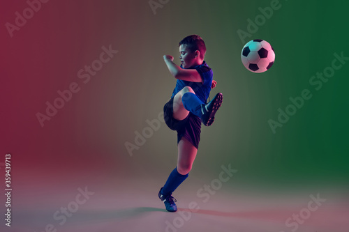 Attacking. Teen male football or soccer player on gradient background in neon light. Caucasian boy training, practicing on the run, in jump. Concept of sport, competition, winning, motion, action. © master1305