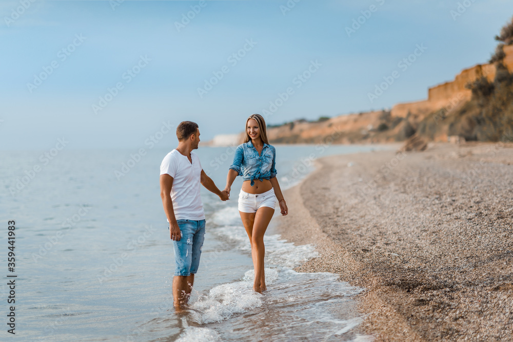 A man and a beautiful woman are enjoying their honeymoon on the beach at sunset. Husband and wife are walking by the ocean. Beautiful young couple spend time together. A man and a beautiful woman are enjoying their honeymoon on the beach at sunset. Husband and wife are walking by the ocean. Beautiful young couple spend time together.
