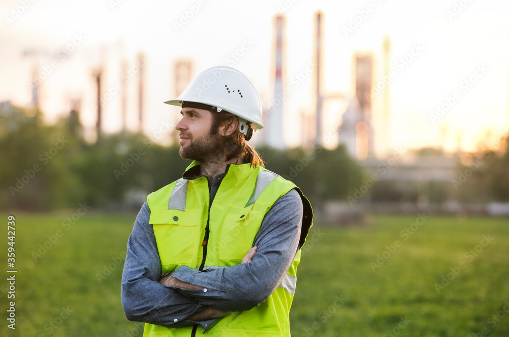 Young engineer standing outdoors by oil refinery, arms crossed. Young engineer standing outdoors by oil refinery, arms crossed.